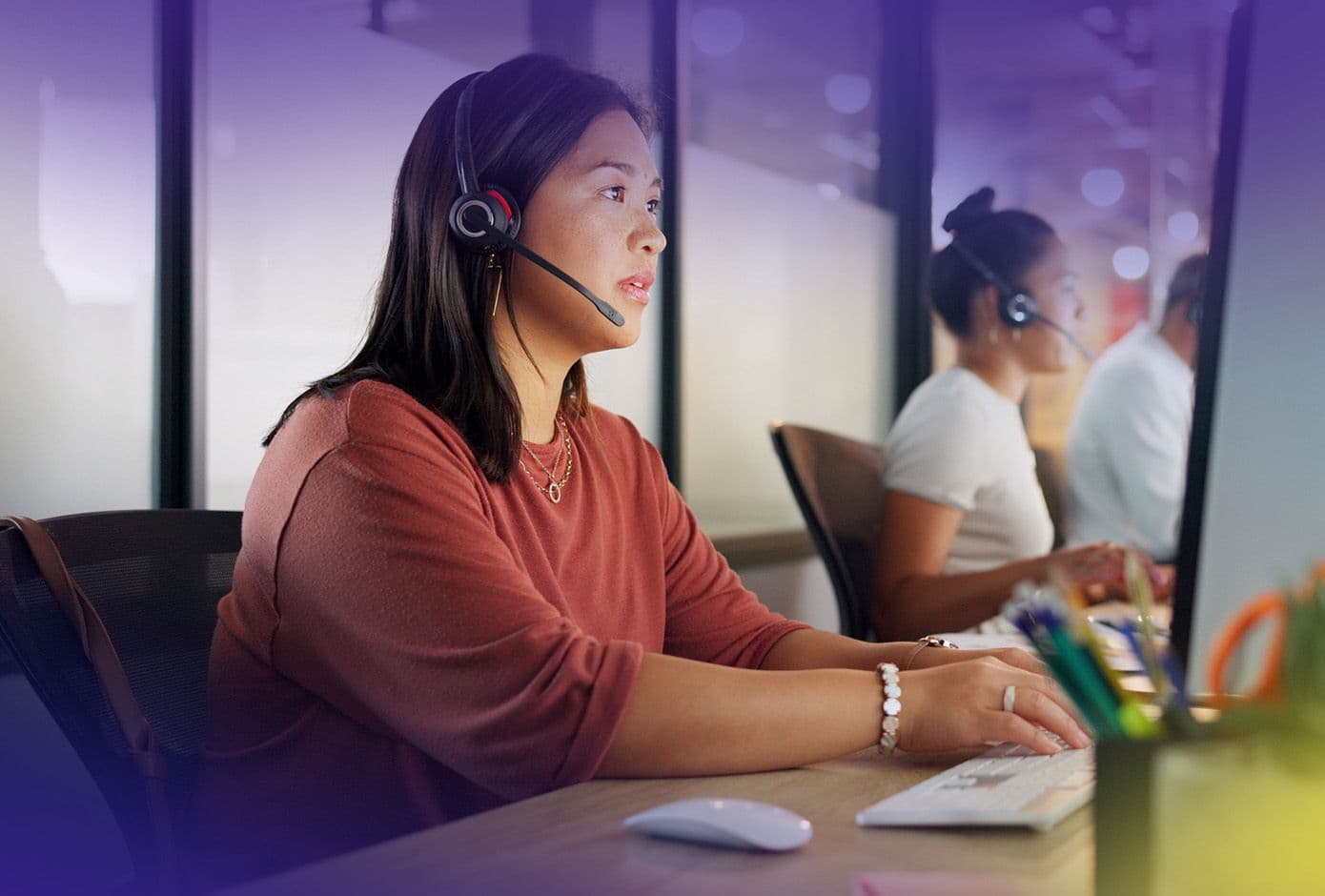 Two women sit at computers with headsets on while on calls.