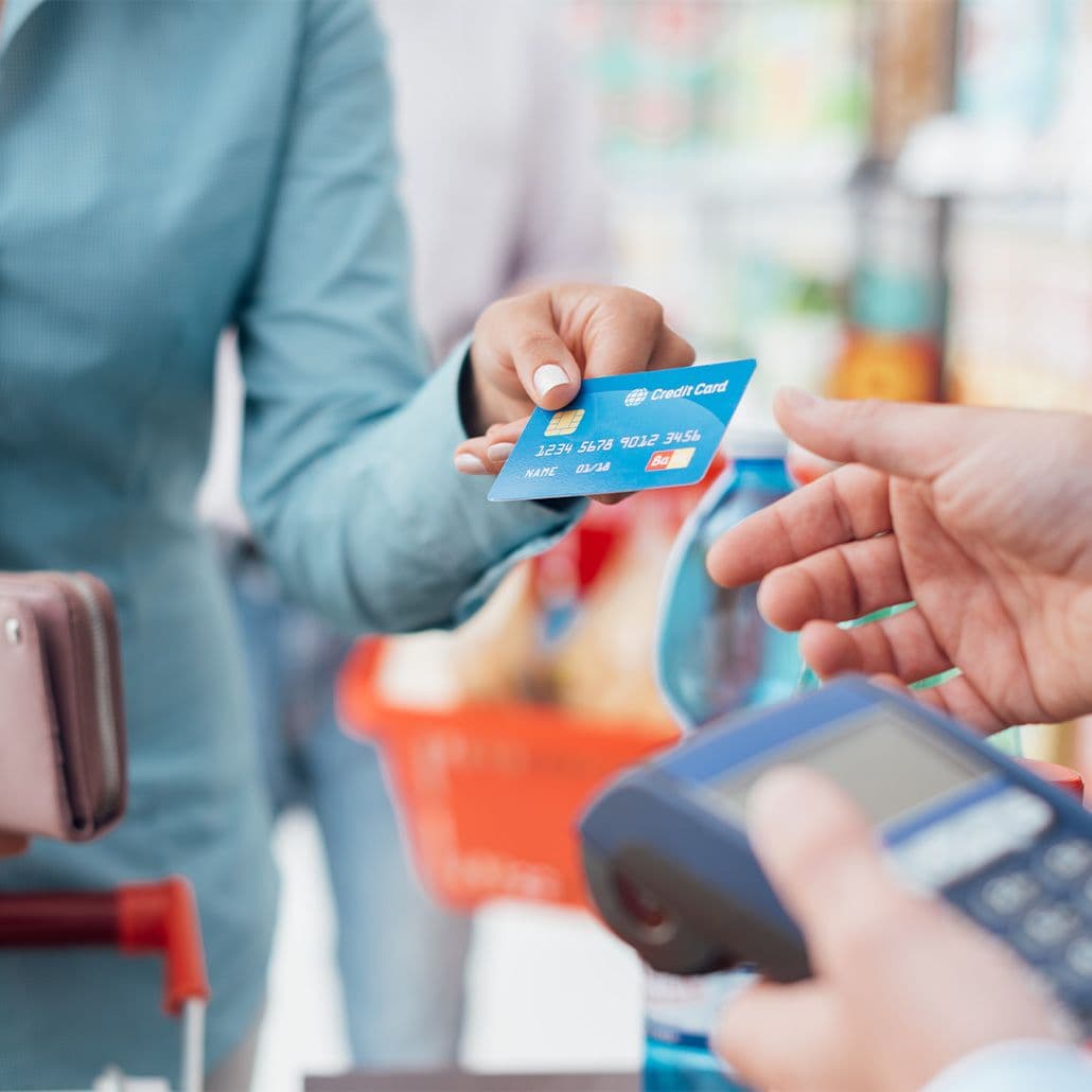 Customer handing credit card to cashier at checkout with payment terminal