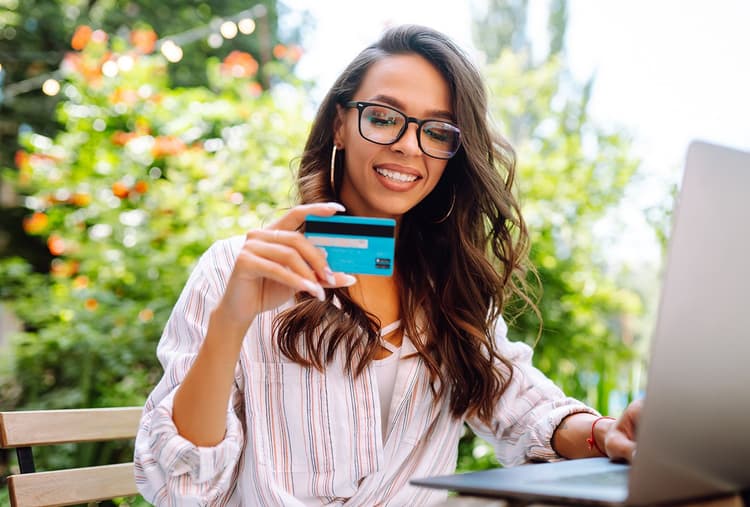 Woman looking at her credit card while sitting in front of her laptop.