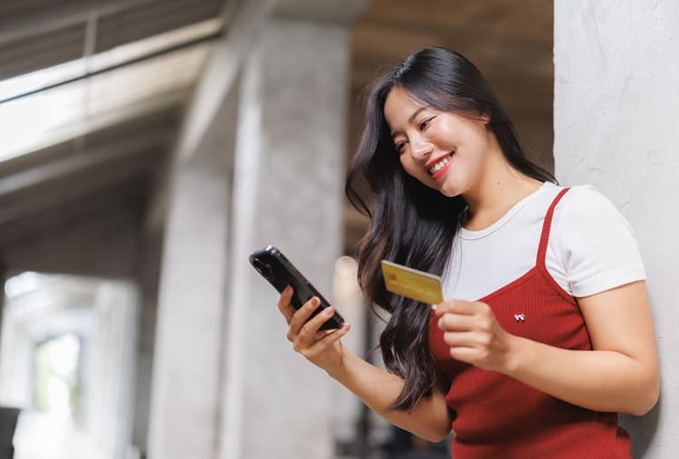 Gen Z woman looks at her phone while holding a credit card.
