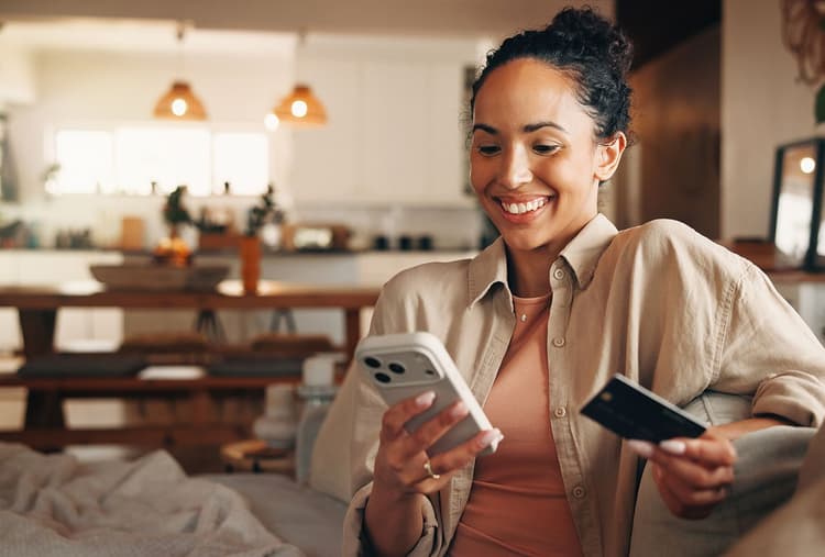 Woman looking at her phone while holding a payment card.